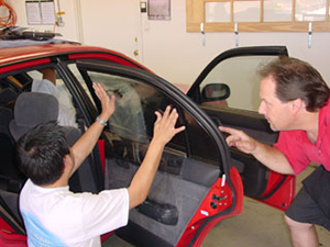Instructor showing student how to apply window tint to the car's front passenger window.